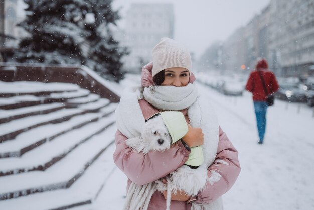 Menina com um cachorro nos braços em uma rua da cidade com neve caindo