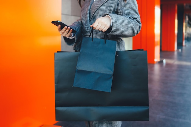 Menina com um telefone nas mãos e sacolas pretas perto de um shopping, sexta-feira negra, hora de venda.