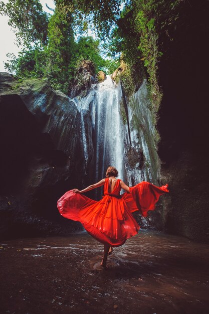 Menina com um vestido vermelho dançando em uma cachoeira.