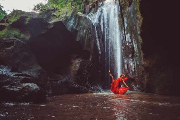 Menina com um vestido vermelho dançando em uma cachoeira.