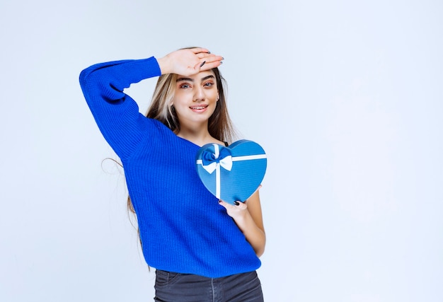 Menina com uma caixa de presente azul parece cansada.