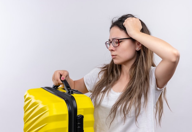 Foto grátis menina com uma camiseta branca segurando uma mala de viagem, parecendo confusa e muito ansiosa tocando a cabeça