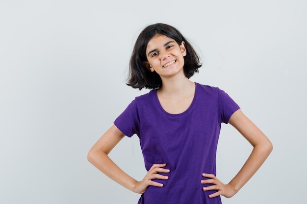 Menina com uma camiseta de mãos dadas na cintura e parecendo alegre,