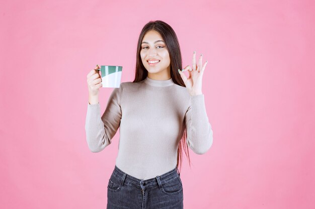 Menina com uma caneca de café fazendo sinal de satisfação