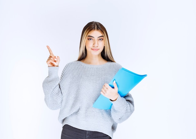 Menina com uma pasta azul apontando para alguém à parte.