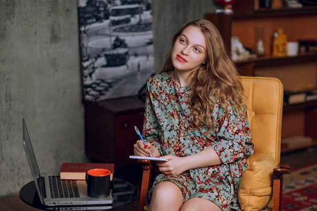 Menina com vestido floral sentado e fazendo anotações em seu caderno.