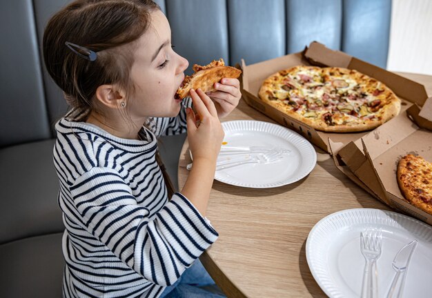 Menina come pizza de queijo apetitosa no almoço.