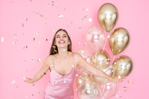 Menina comemorando ano novo ou feliz aniversário com balões de ar em um vestido brilhante jogando confete Foto Premium
