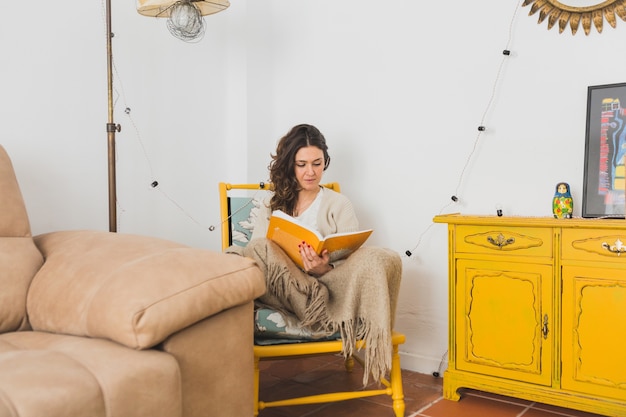 Foto grátis menina concentrada lendo um livro sentada numa cadeira amarela