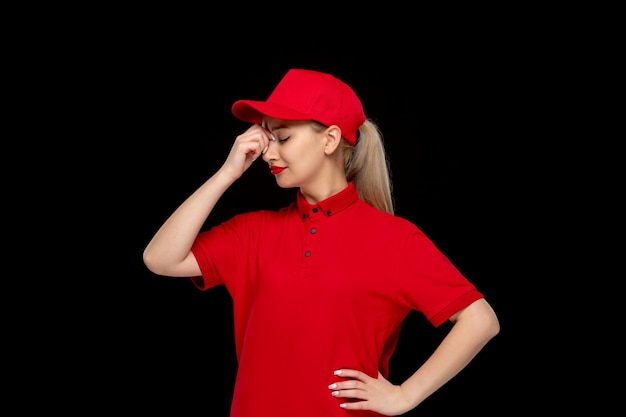 Menina confusa do dia da camisa vermelha tocando a testa em um boné vermelho vestindo camisa e batom brilhante