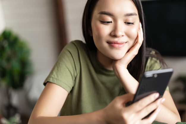 Menina coreana sorridente em camiseta verde, olhando para o telefone móvel pedido smth no aplicativo de compras de ...