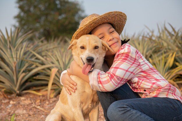 menina criança asiática e cachorro. Feliz linda garota de jeans em geral e chapéu brincando com o cachorro na fazenda de abacaxi, verão na zona rural, infância e sonhos, estilo de vida ao ar livre.