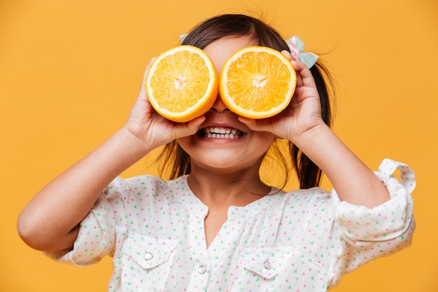 Menina criança cobrindo os olhos com laranja.