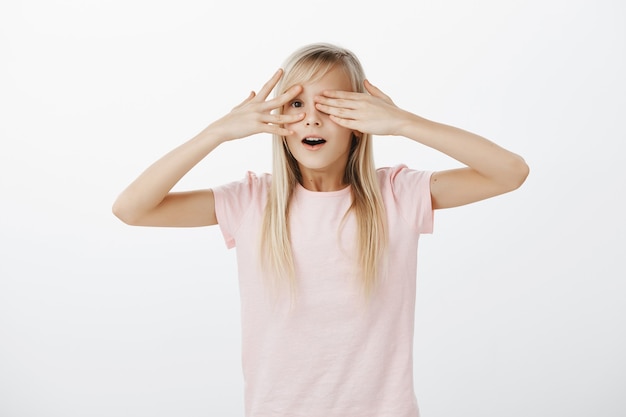 Menina curiosa e fofa espiando por entre os dedos