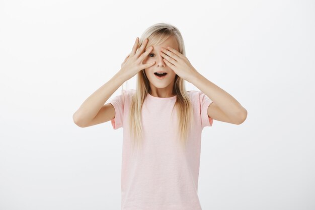 Menina curiosa e fofa espiando por entre os dedos