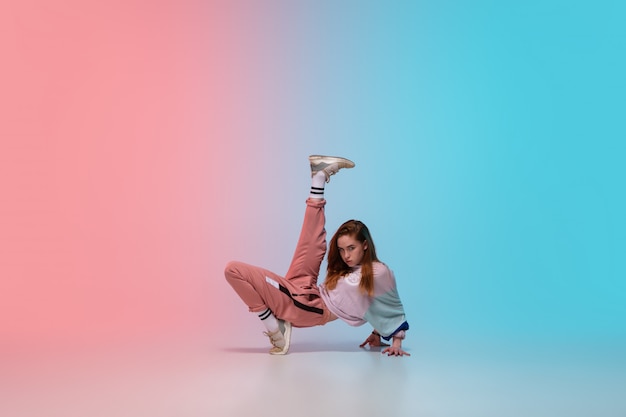 Menina dançando hip-hop em roupas elegantes em fundo gradiente no salão de dança na luz de neon.