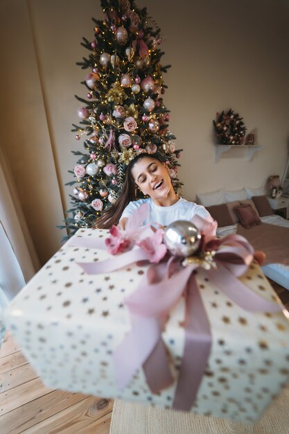 Menina dando um presente no fundo de uma árvore de Natal