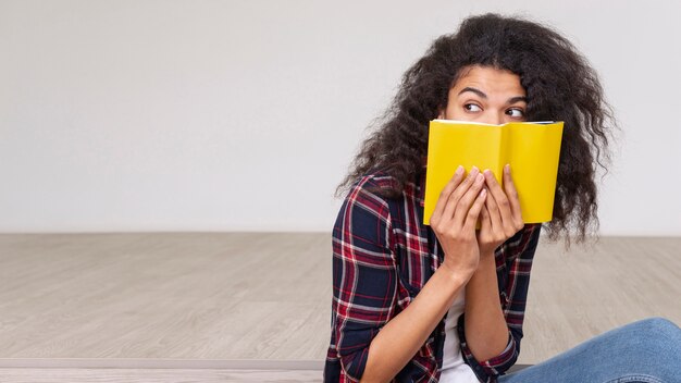 Menina de alto ângulo, cobrindo o rosto com o livro