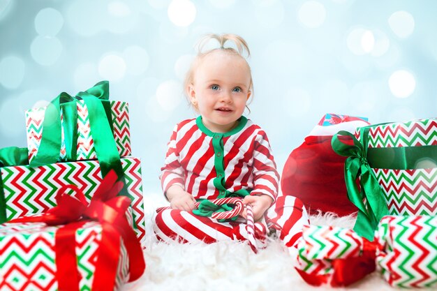 Menina de bebê fofo 1 ano de idade perto de chapéu de Papai Noel, posando no Natal com decoração. Sentado no chão com uma bola de natal