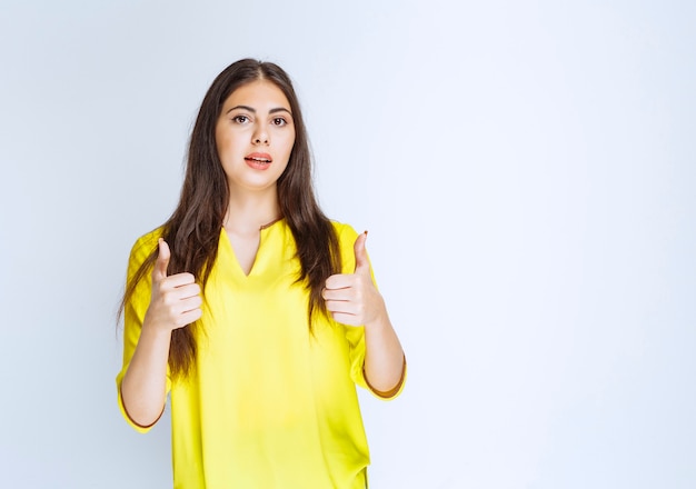 Menina de camisa amarela, mostrando o polegar para cima o sinal.