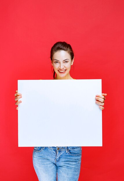 Menina de camisa amarela segurando um quadro de informações quadrado