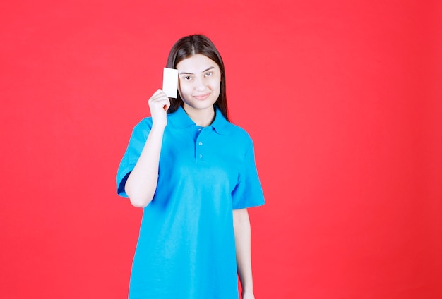 Menina de camisa azul, apresentando seu cartão de visita e parece pensativa.