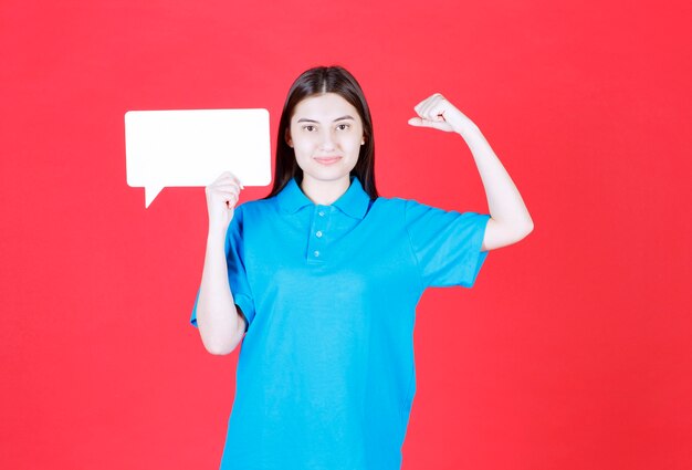 Menina de camisa azul segurando um quadro retangular de informações e mostrando um sinal positivo