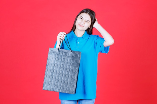 Menina de camisa azul segurando uma sacola roxa de compras parecendo confusa e pensativa