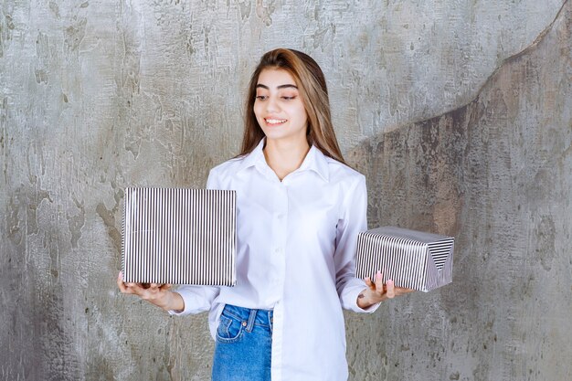 Menina de camisa branca segurando caixas de presente de prata.