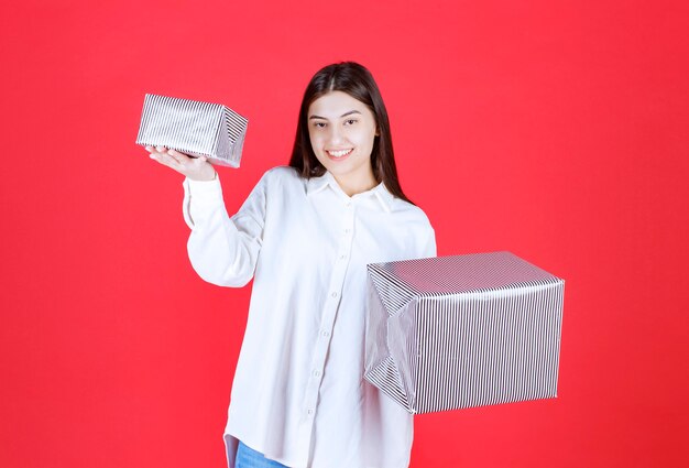 Menina de camisa branca segurando duas caixas de presente prateadas com as duas mãos e fazendo uma escolha