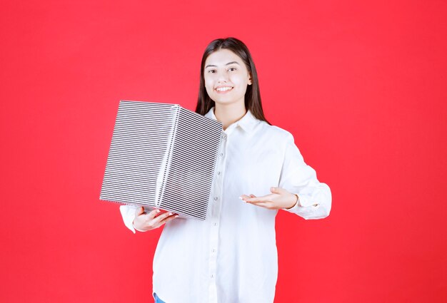 Menina de camisa branca segurando uma caixa de presente prateada