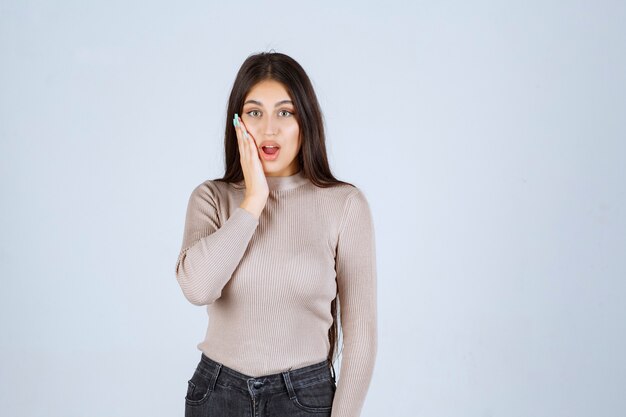 Menina de camisa cinza parece animada e surpresa.