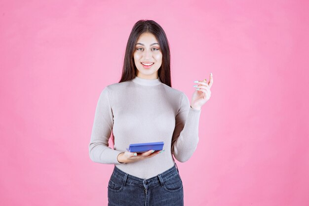 Menina de camisa cinza segurando uma calculadora azul e sorrindo com confiança