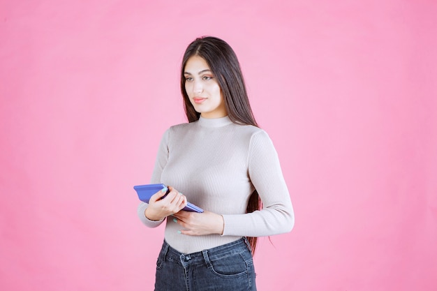 Menina de camisa cinza segurando uma calculadora azul, observando e trabalhando com ela