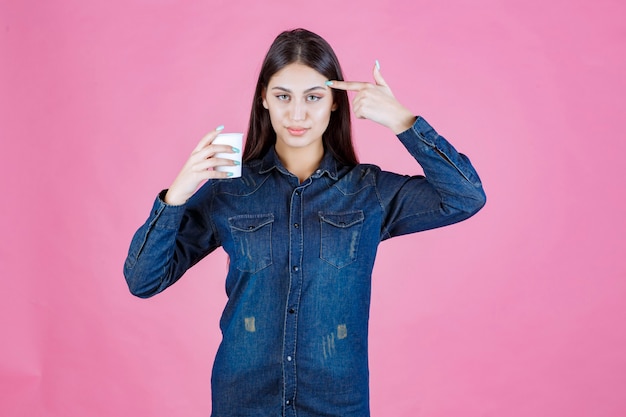 Menina de camisa jeans segurando uma xícara de café e pensando