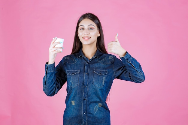 Menina de camisa jeans tomando café e levantando o polegar