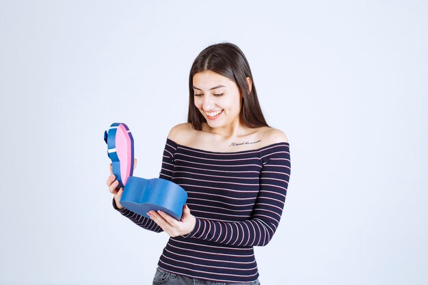 Menina de camisa listrada abre uma caixa de presente azul e fica surpresa.