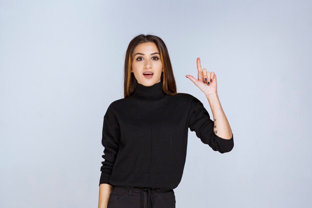 Menina de camisa preta apontando acima. Foto de alta qualidade