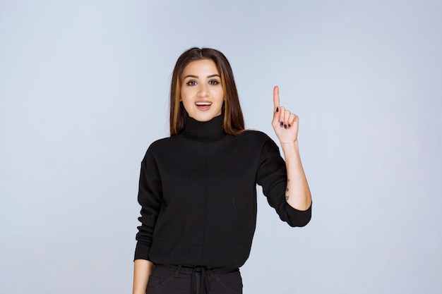 Menina de camisa preta apontando acima. Foto de alta qualidade