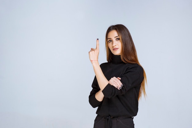 Menina de camisa preta apontando acima. Foto de alta qualidade