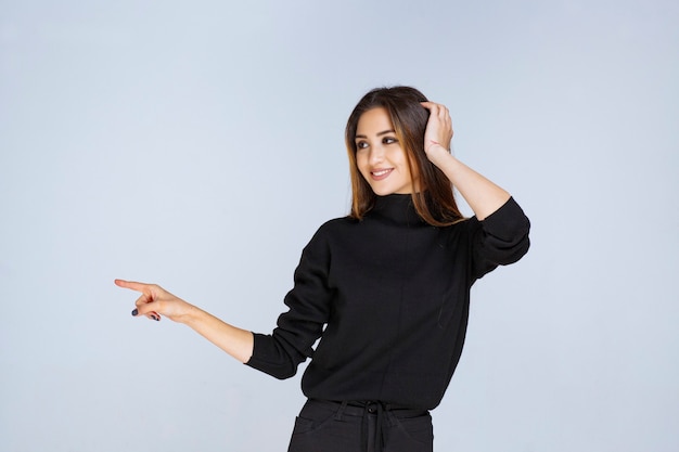 Menina de camisa preta apontando para algo à esquerda. Foto de alta qualidade