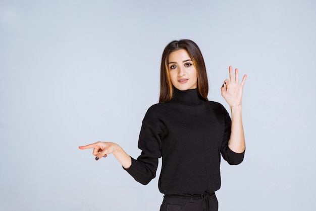 Menina de camisa preta, mostrando sinal positivo com a mão. Foto de alta qualidade