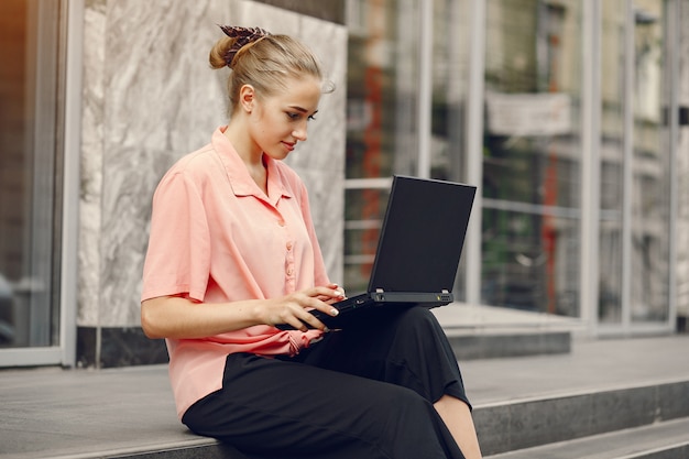 Menina de camisa rosa, sentado perto de casa e usar o laptop