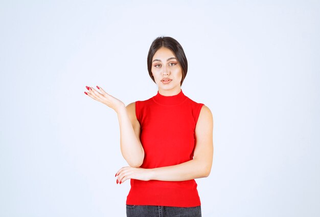 Menina de camisa vermelha, apontando para algo à esquerda.