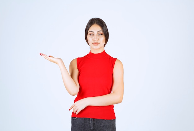 Menina de camisa vermelha, apontando para algo à esquerda.