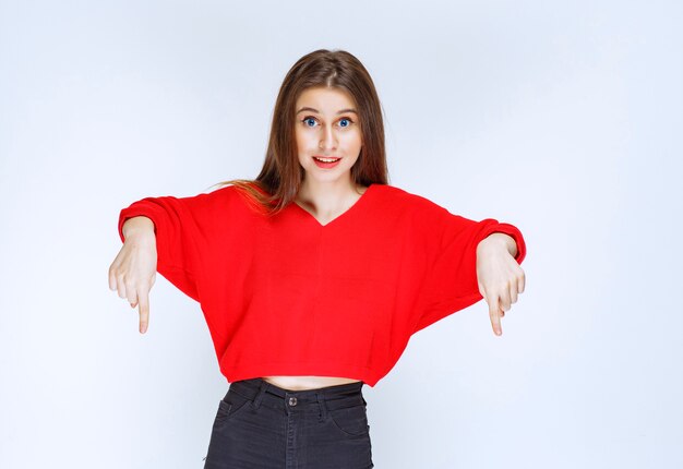 Menina de camisa vermelha, apontando para algo atrás.