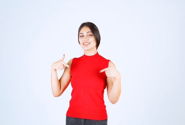 Menina de camisa vermelha, apontando para si mesma.