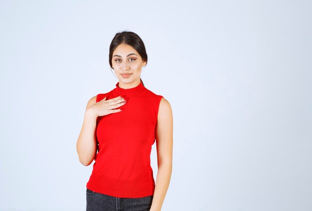 Menina de camisa vermelha, apontando para si mesma.