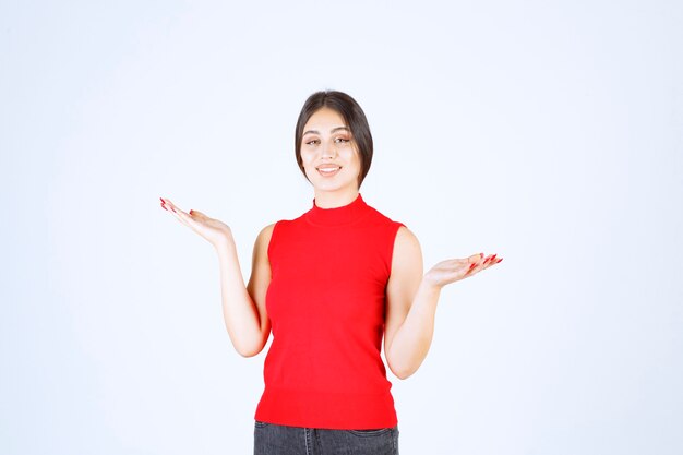 Menina de camisa vermelha, mostrando algo na mão aberta.