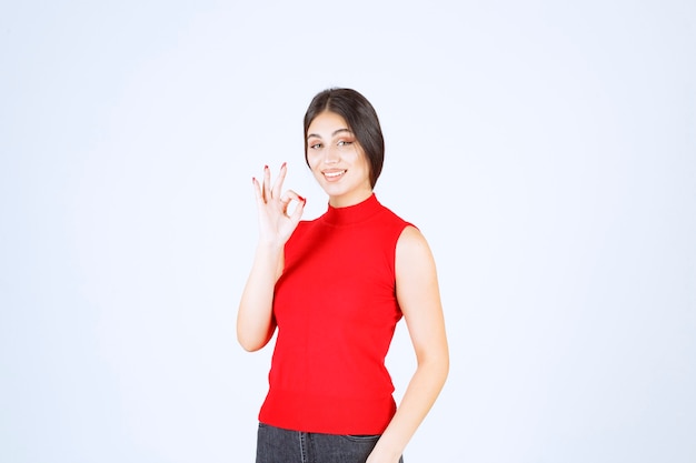 Menina de camisa vermelha, mostrando sinal positivo com a mão.